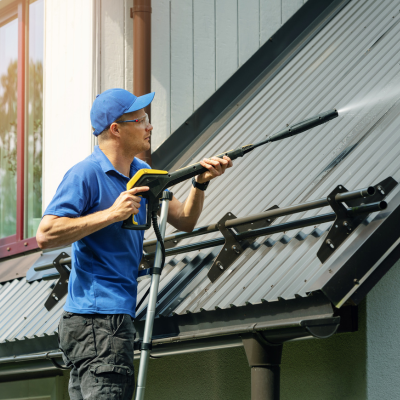 A man in a blue shirt and cap operates a pressure washer to clean a roof in Port Royal, South Carolina.